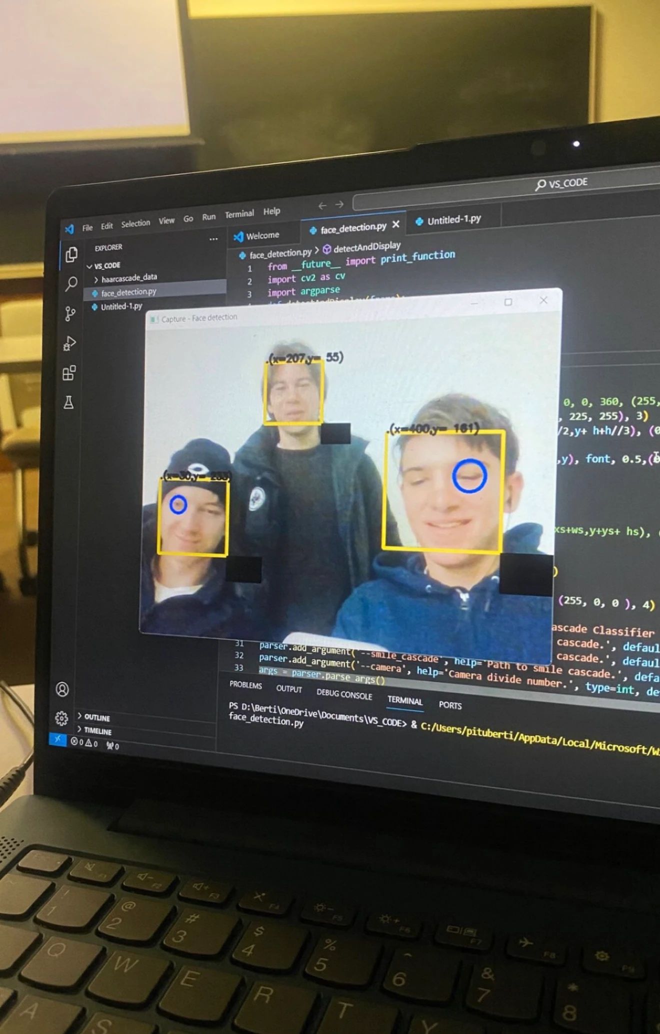 A laptop running face-detection software, with three faces outlined on screen.