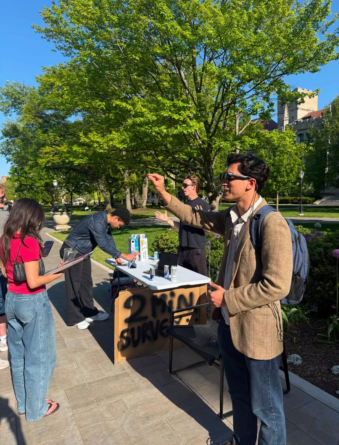 People trying glasses and talking around a table in a sunny campus quad.
